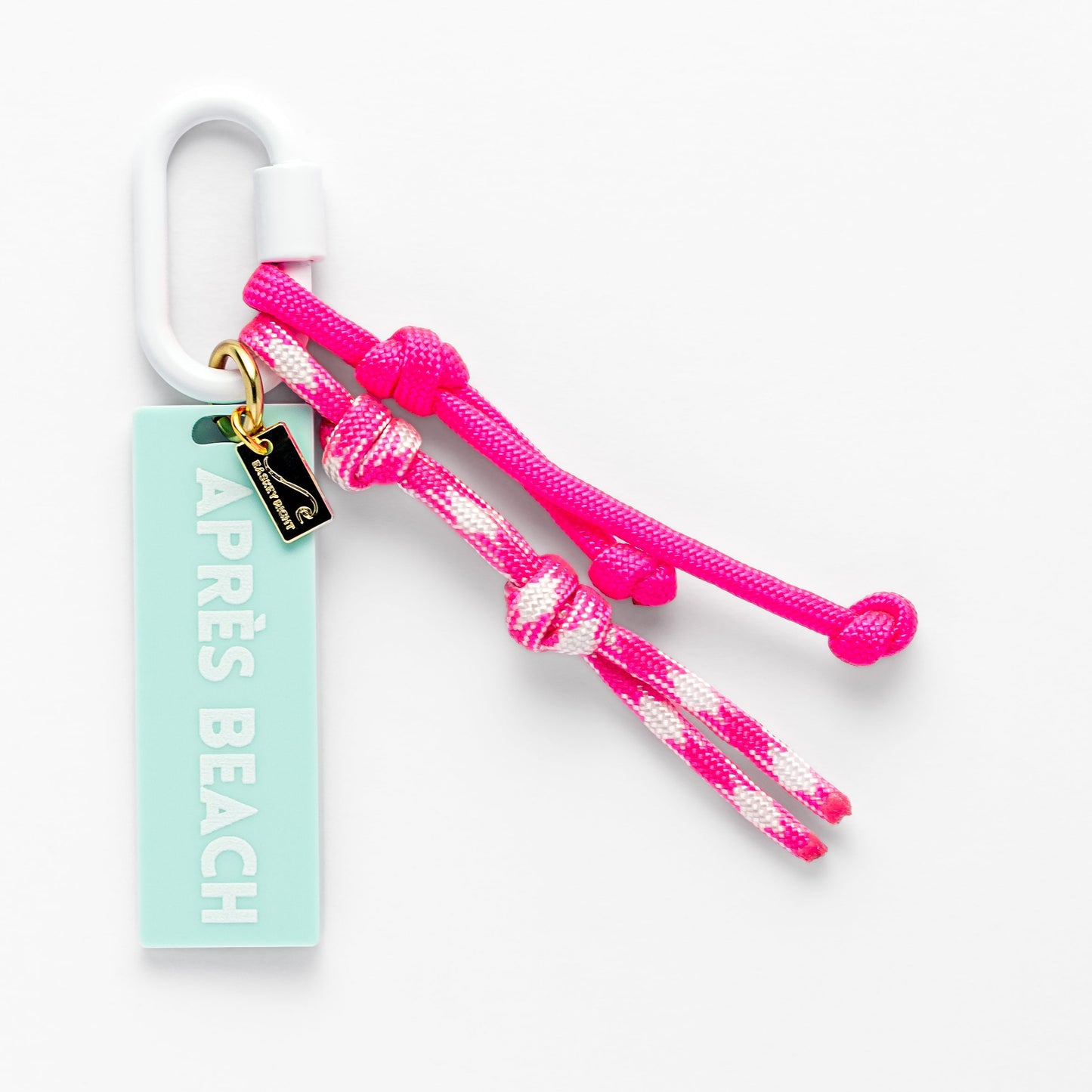 Pink and white braided bag charm with a tag labeled 'Apres Beach' on a white background